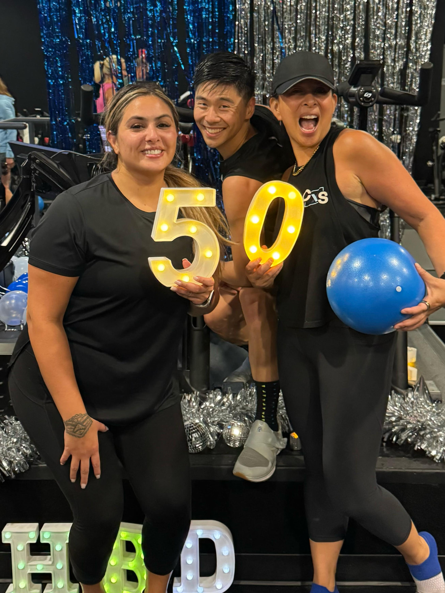 Three members holding a lit 50 at a birthday celebration in the cycling theater