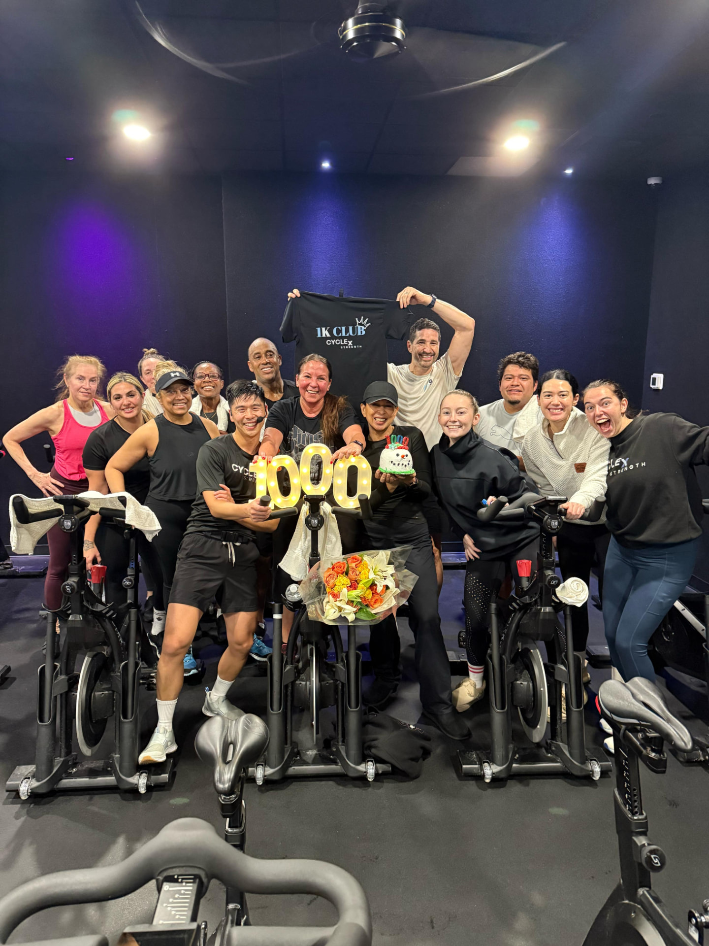 A full class celebrating a member's 1,000th ride with a 1K Club shirt