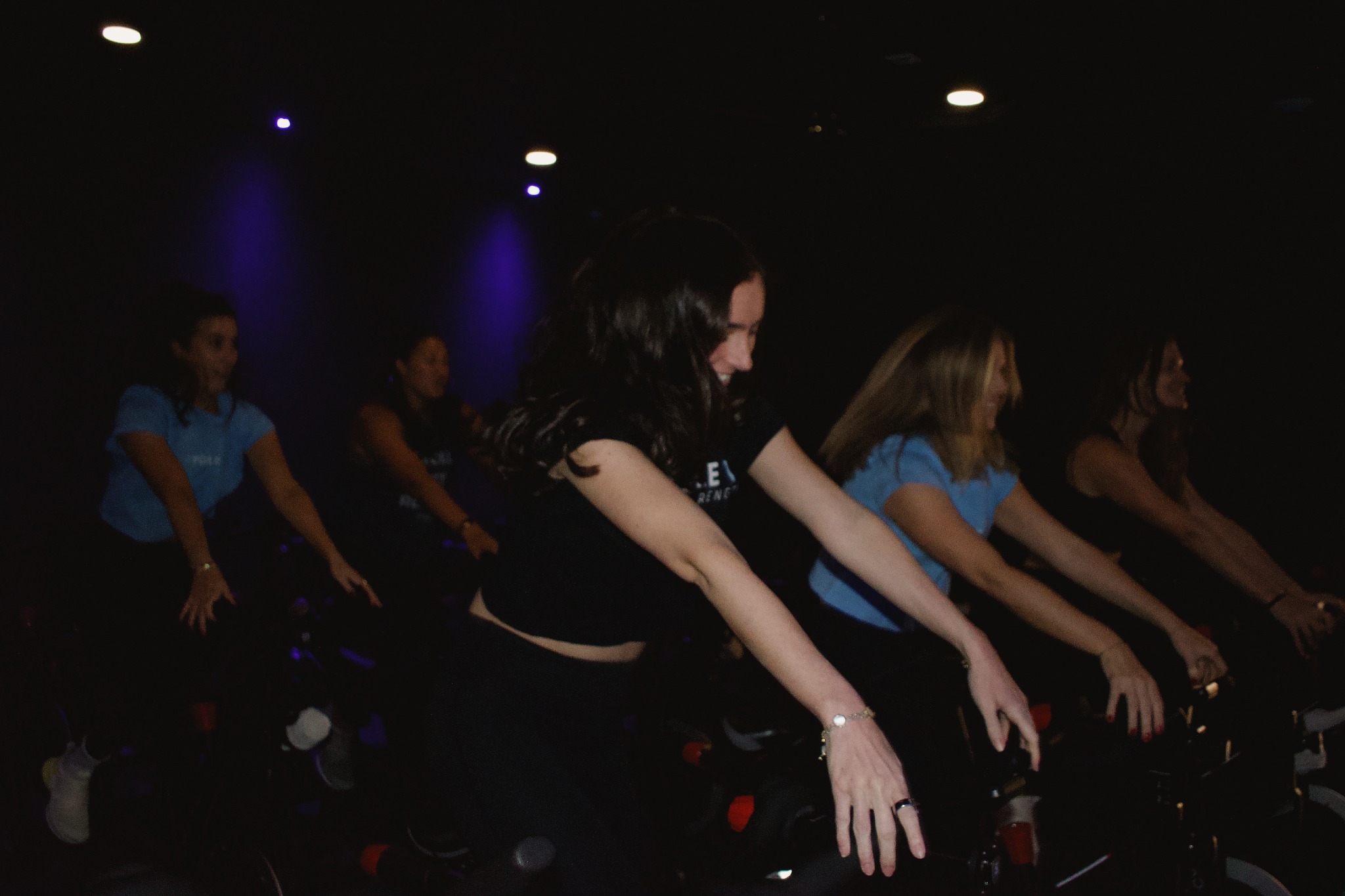Riders side by side on their bikes during an indoor cycling class in the dark theater