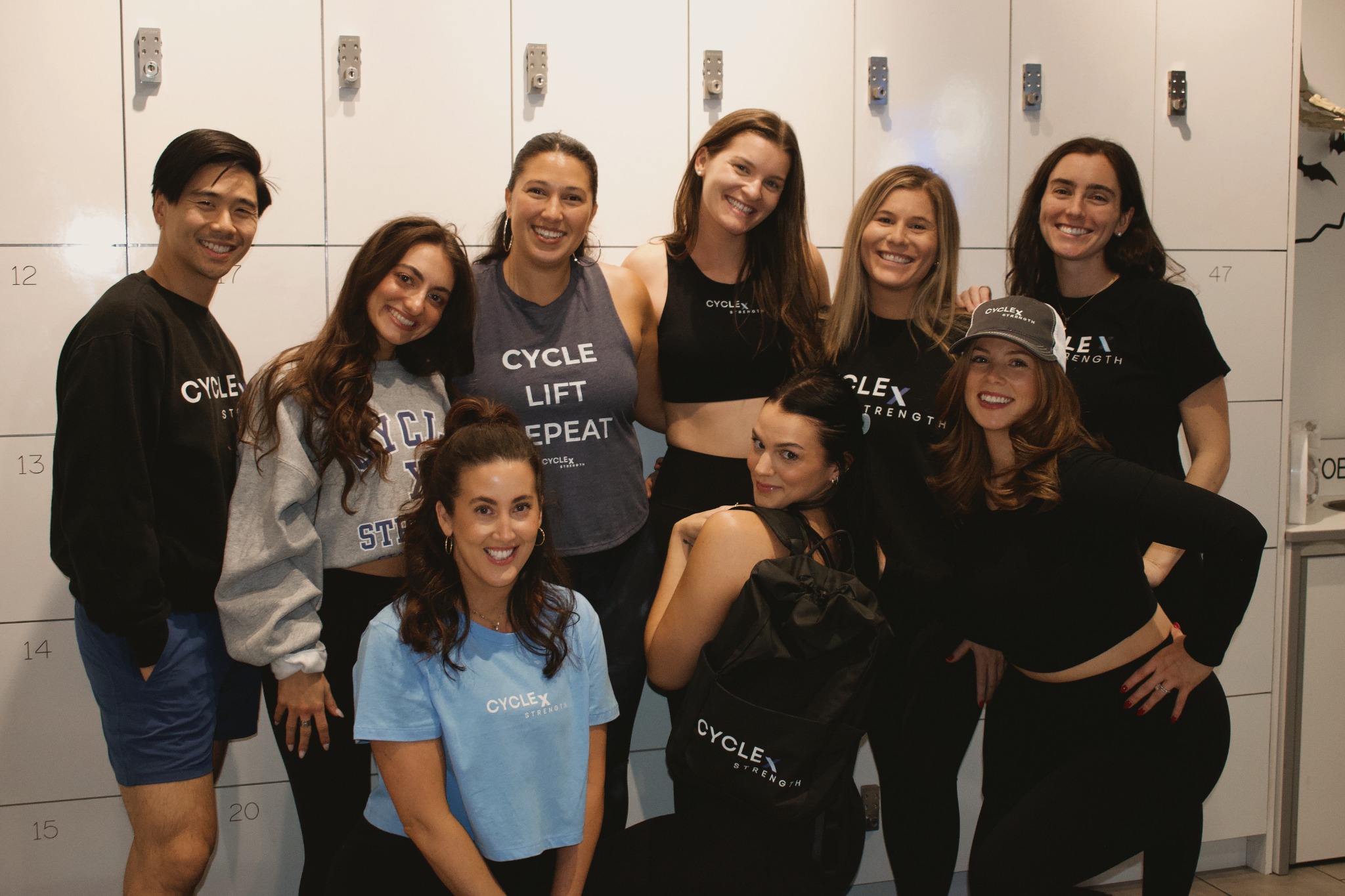 Nine Cycle x Strength instructors together in front of studio lockers, wearing CxS apparel.